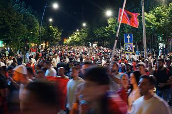 Une manifestation, de nuit, sur laquelle flotte un drapeau albanais.