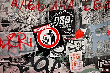 Un mur avec des stickers et des gribouillis. Au milieu, un sticker avec un bonhomme qui jette quelque chose dans une poubelle avec écrit "Scheiss AFD !"