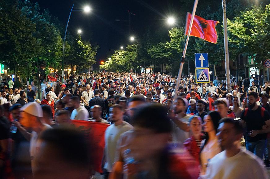 Une manifestation, de nuit, sur laquelle flotte un drapeau albanais.